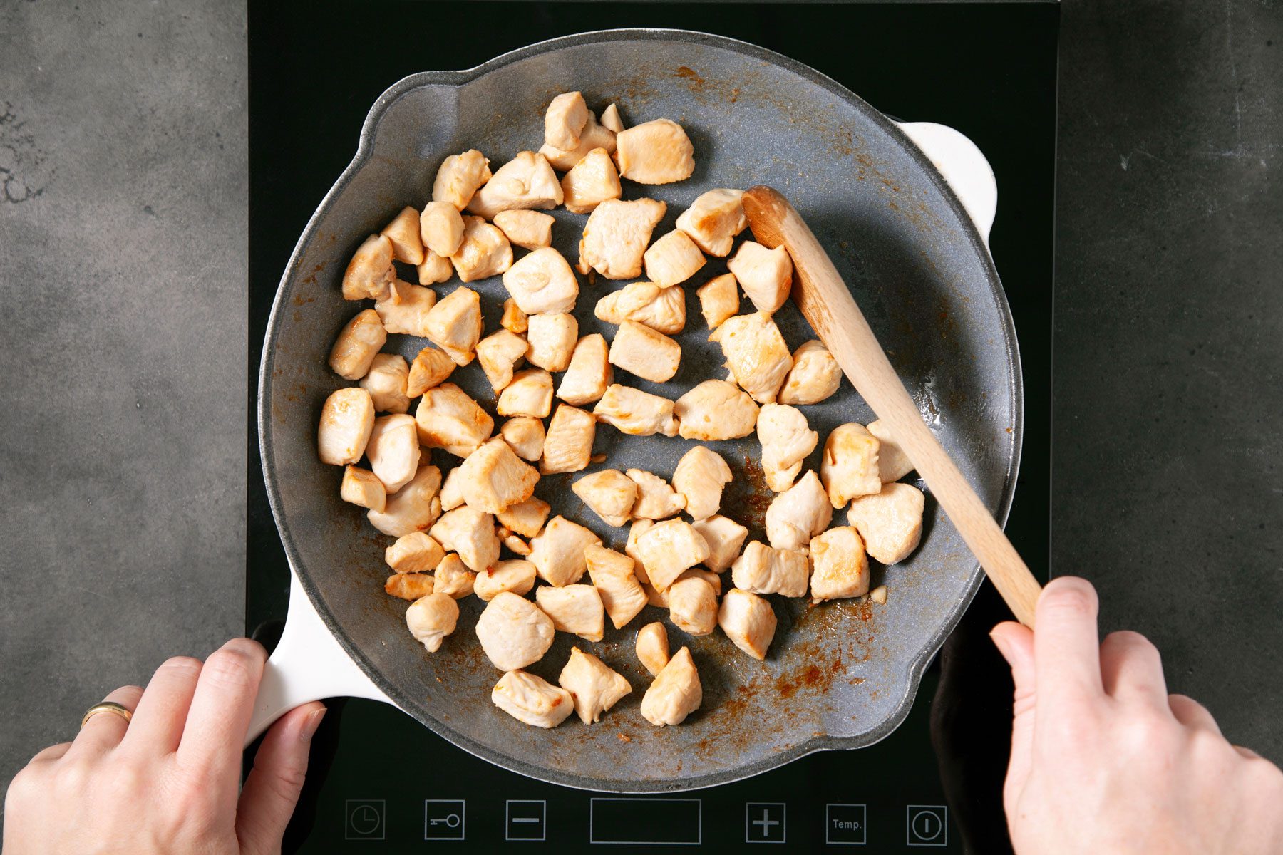 A person cooking Chicken in a small skillet