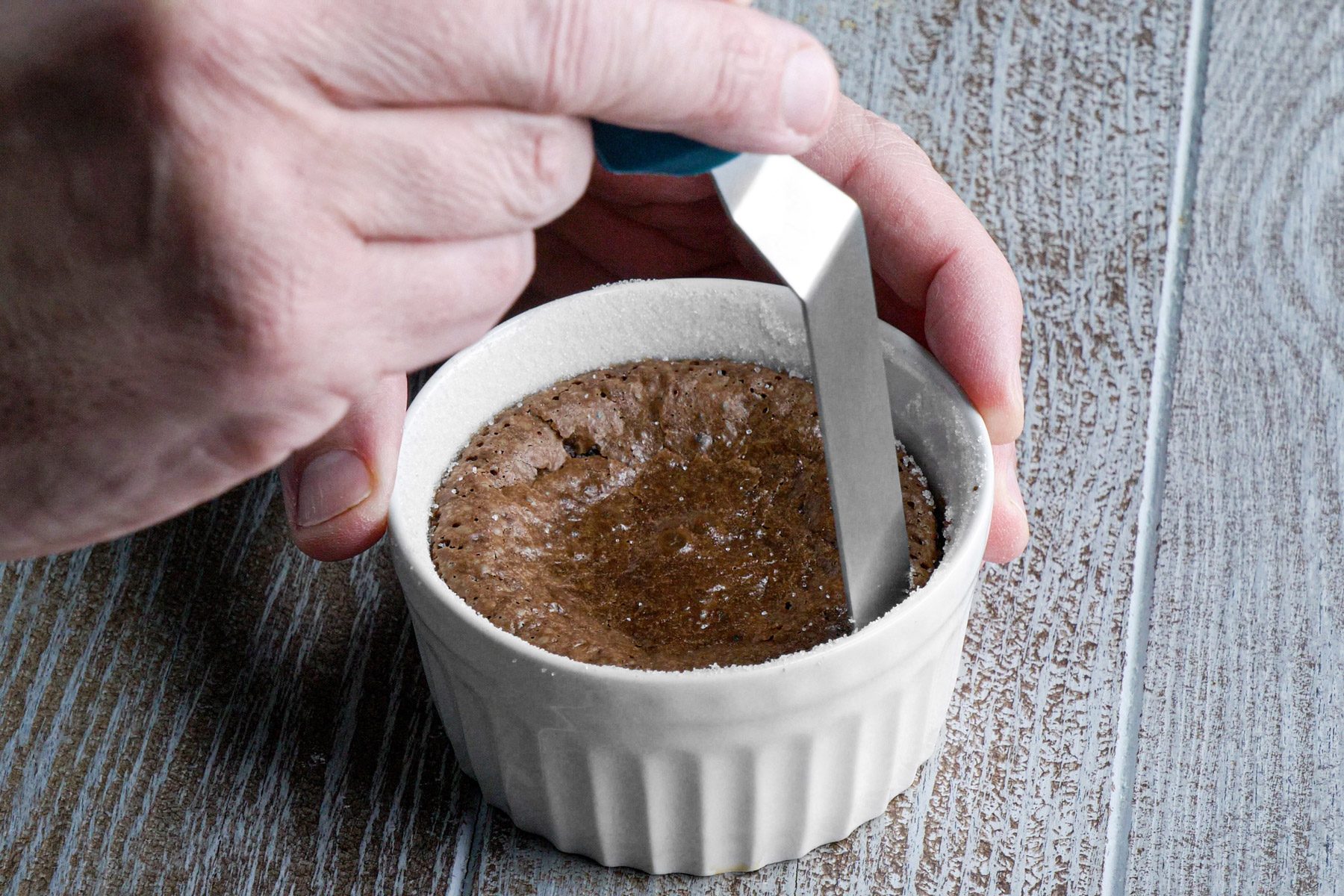A person holding a knife over a white ramekin