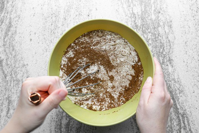 A person whisking flour, baking cocoa in a large bowl.