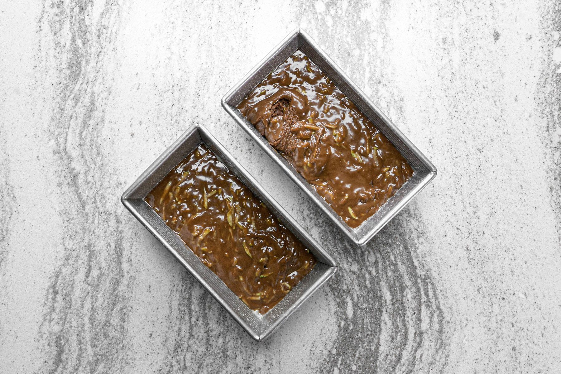 Chocolate batter in a loaf pans on a marble countertop.