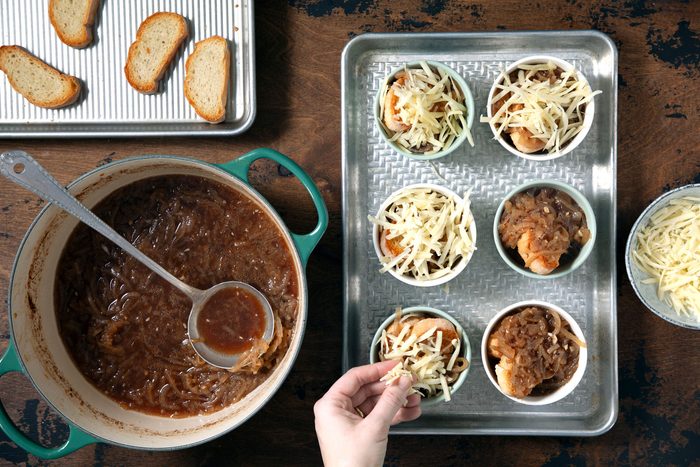 Topping the cheese over the toast and onion soup inside small cups