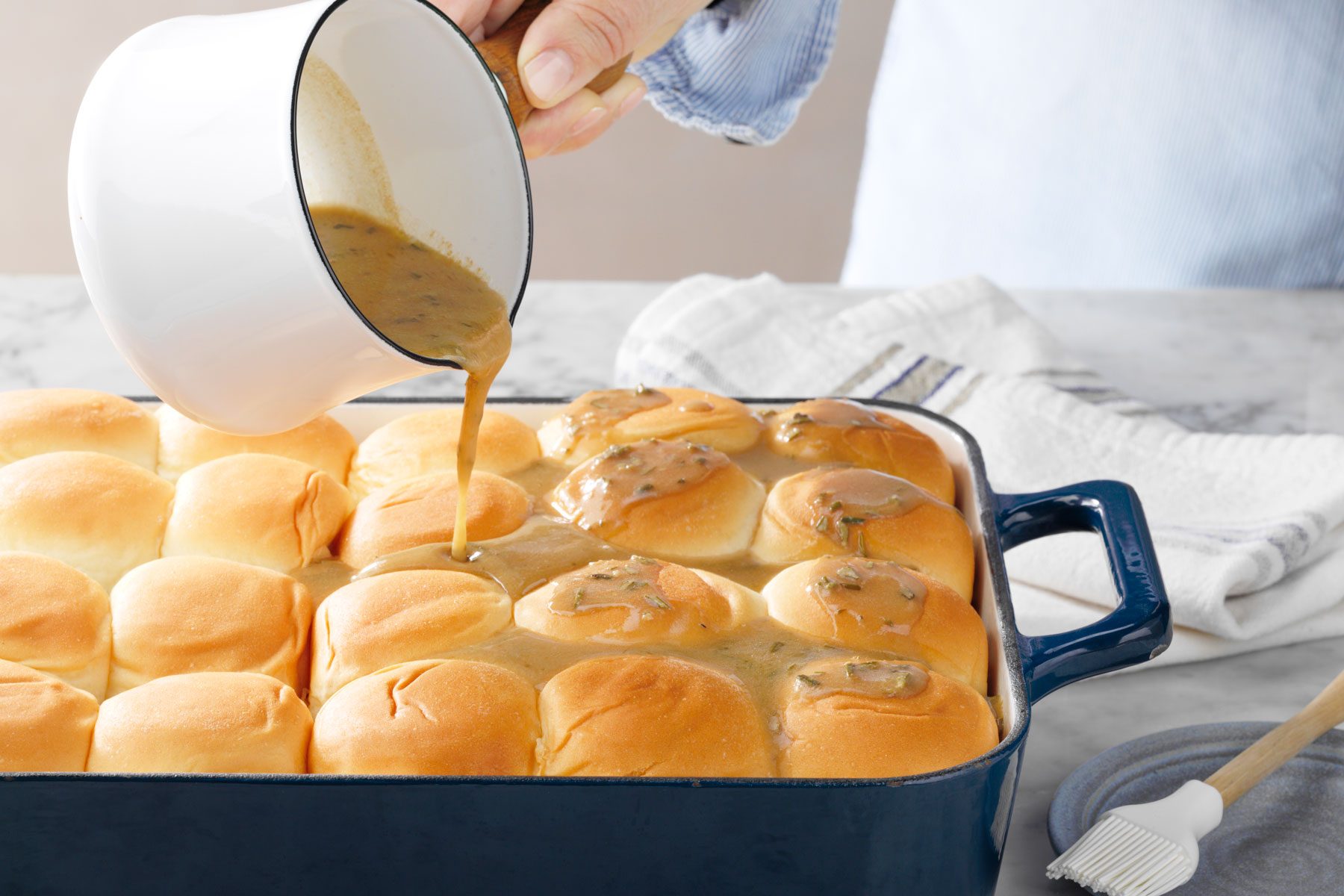 A person drizzling butter on buns