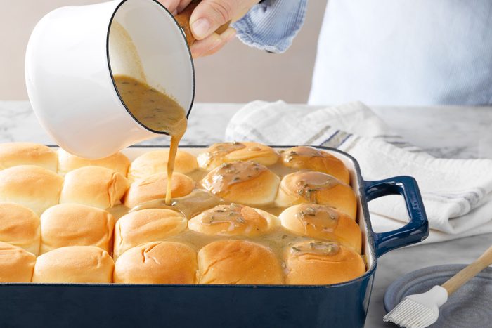 A person drizzling butter on buns