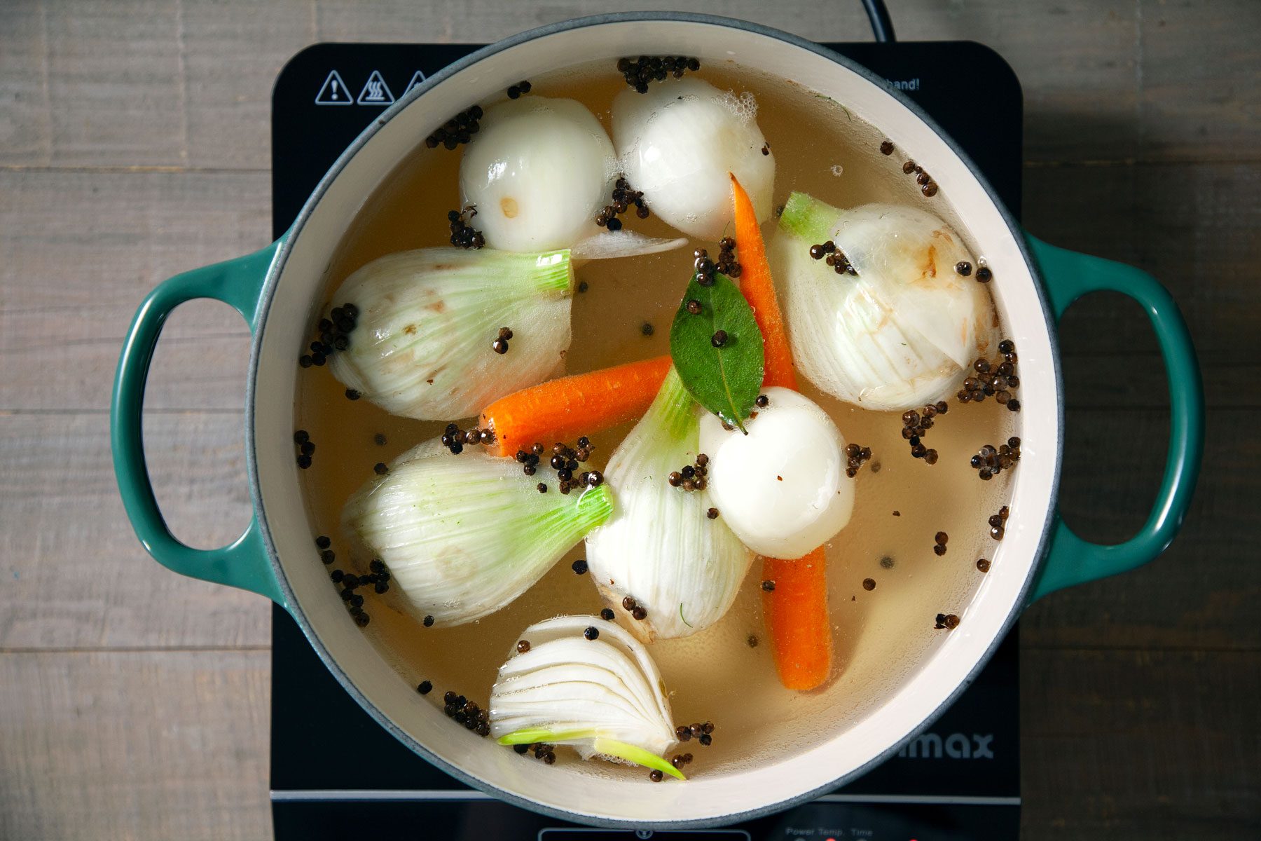 Water, oil, onion, carrot, fennel and peppercorns mixed in a Dutch oven