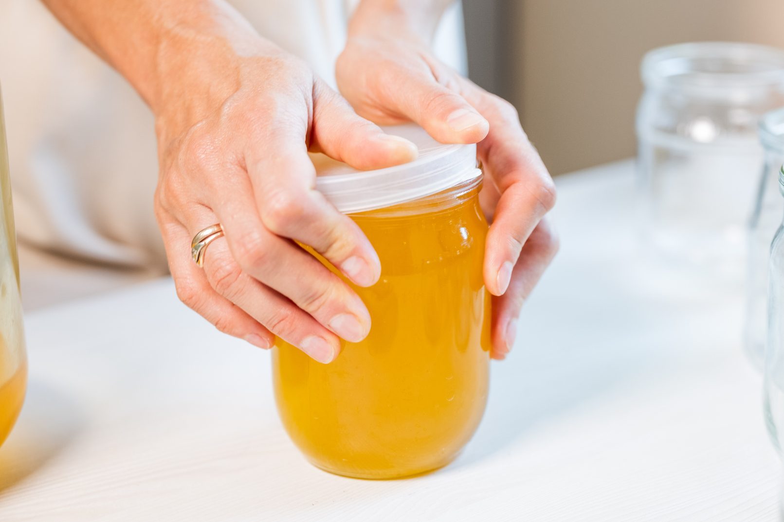 Woman's hands close the lid of a jar of honey standing on a white table and next to a saucer with a spoon