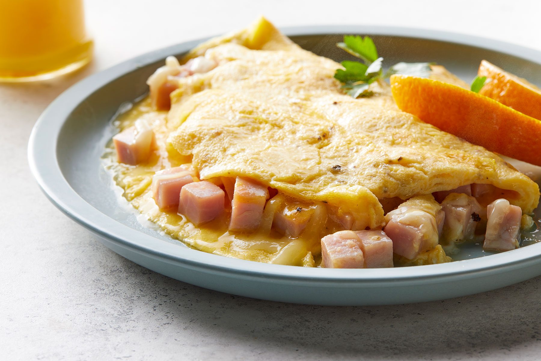 Ham And Cheese Omelet served on plate with orange slices and juice glass on side