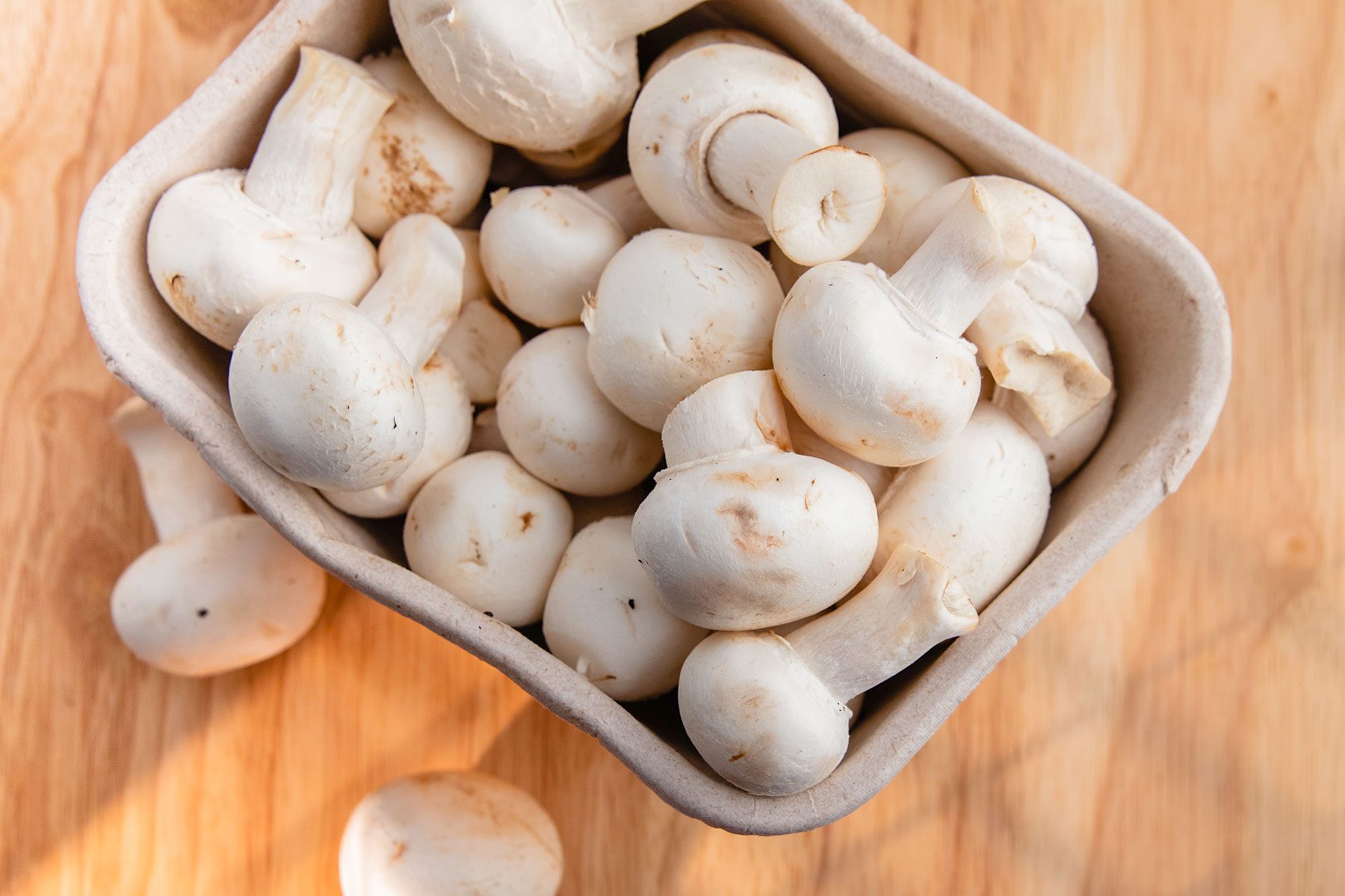 Cardboard containers of white mushroom. Wooden board. Light effect. High point of view.