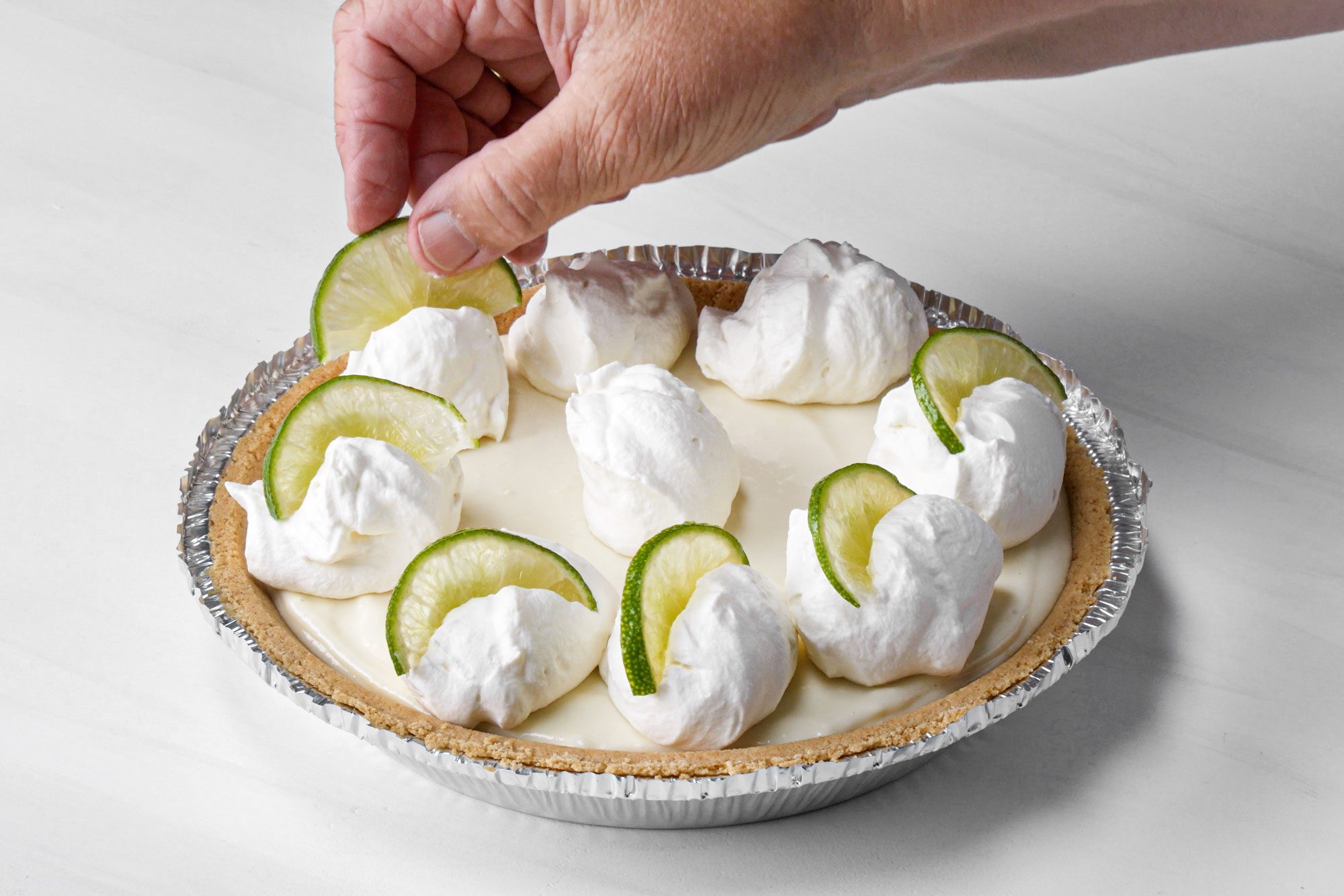 a person topping the pie with whipped cream and lemon slices on marble surface