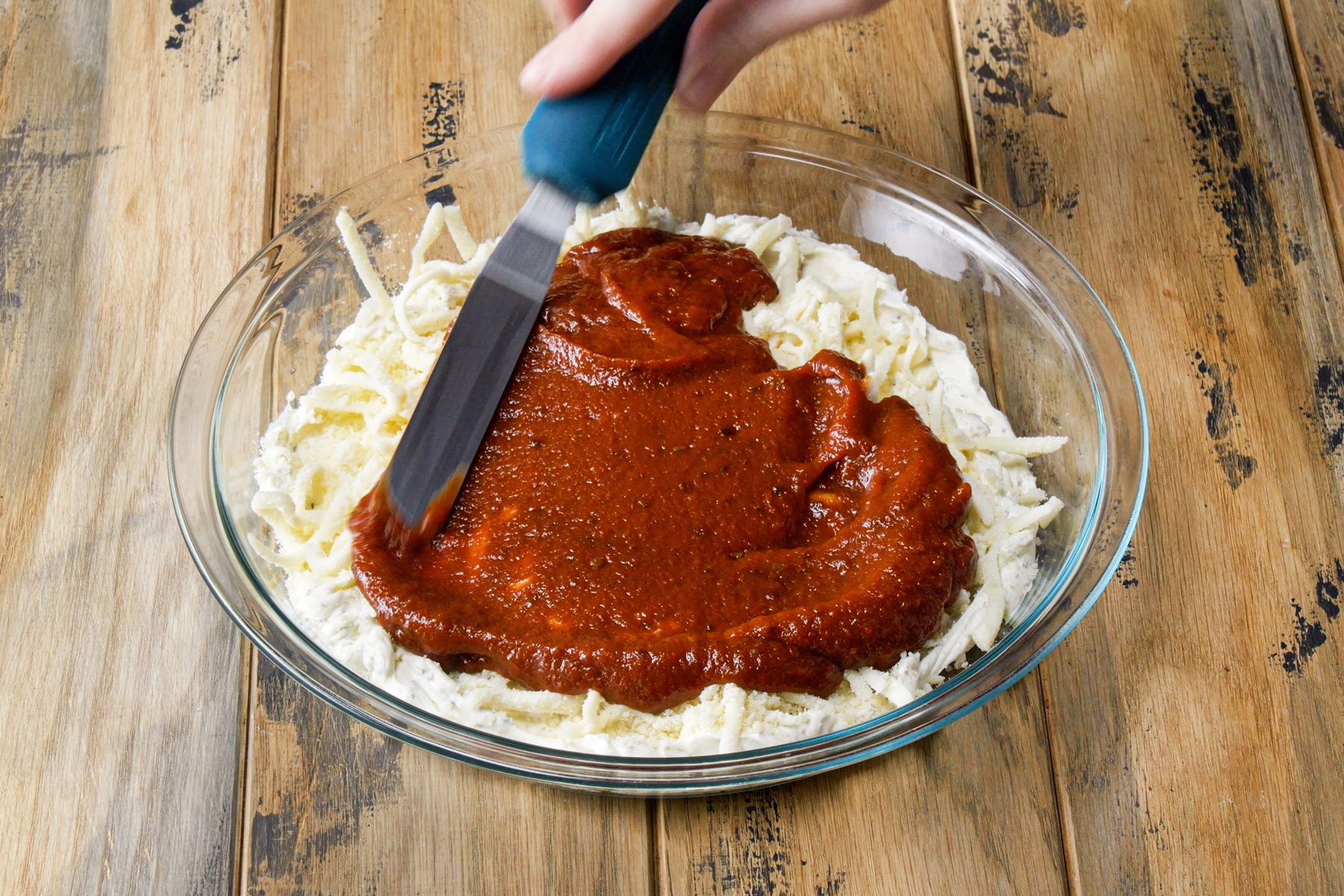 Spreading pizza sauce on the cheese and cream