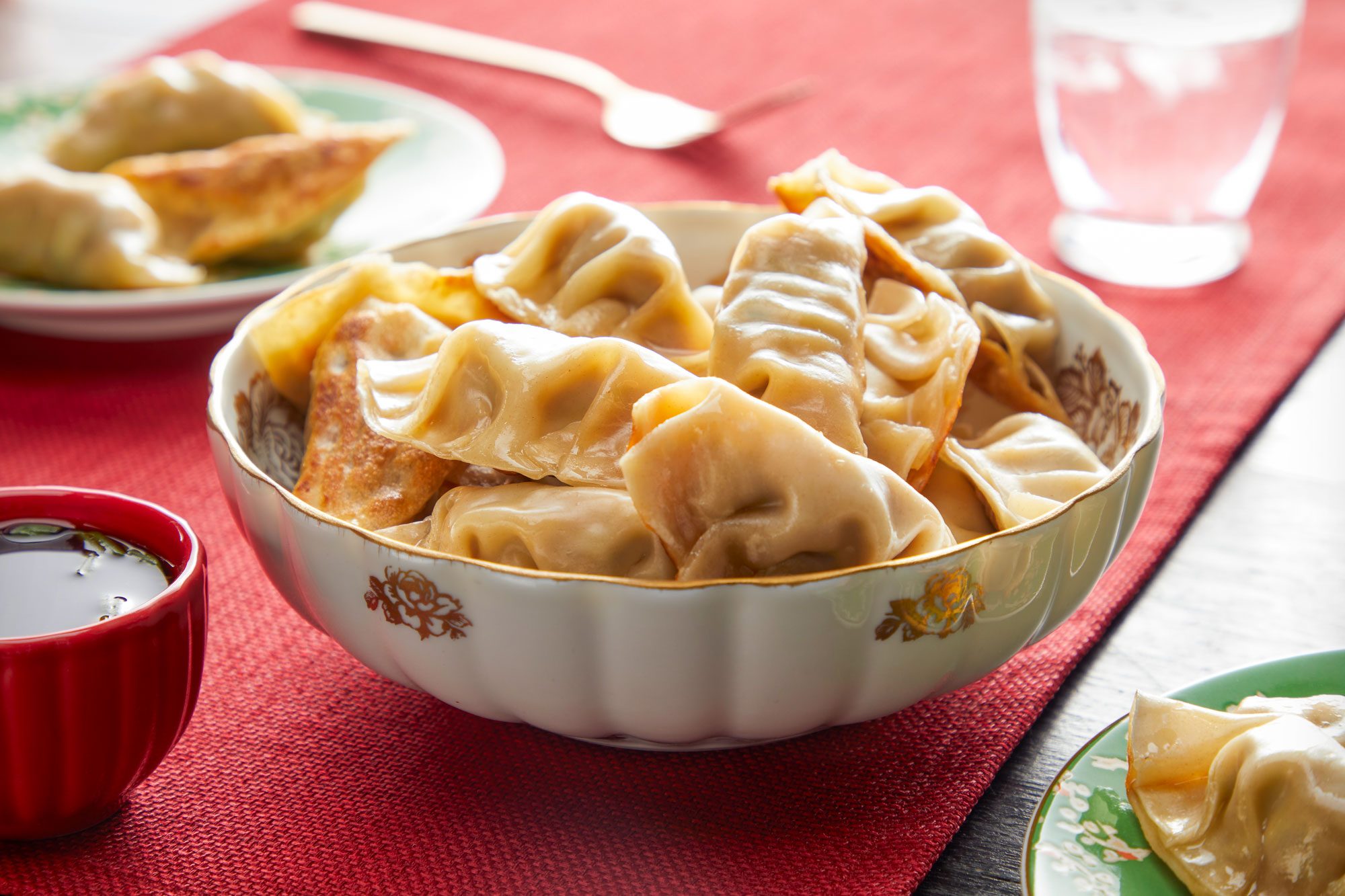 Pork Dumplings in a Japanese Style Bowl and Soy Sauce in a Small Bowl on Red Cloth on Wooden Surface