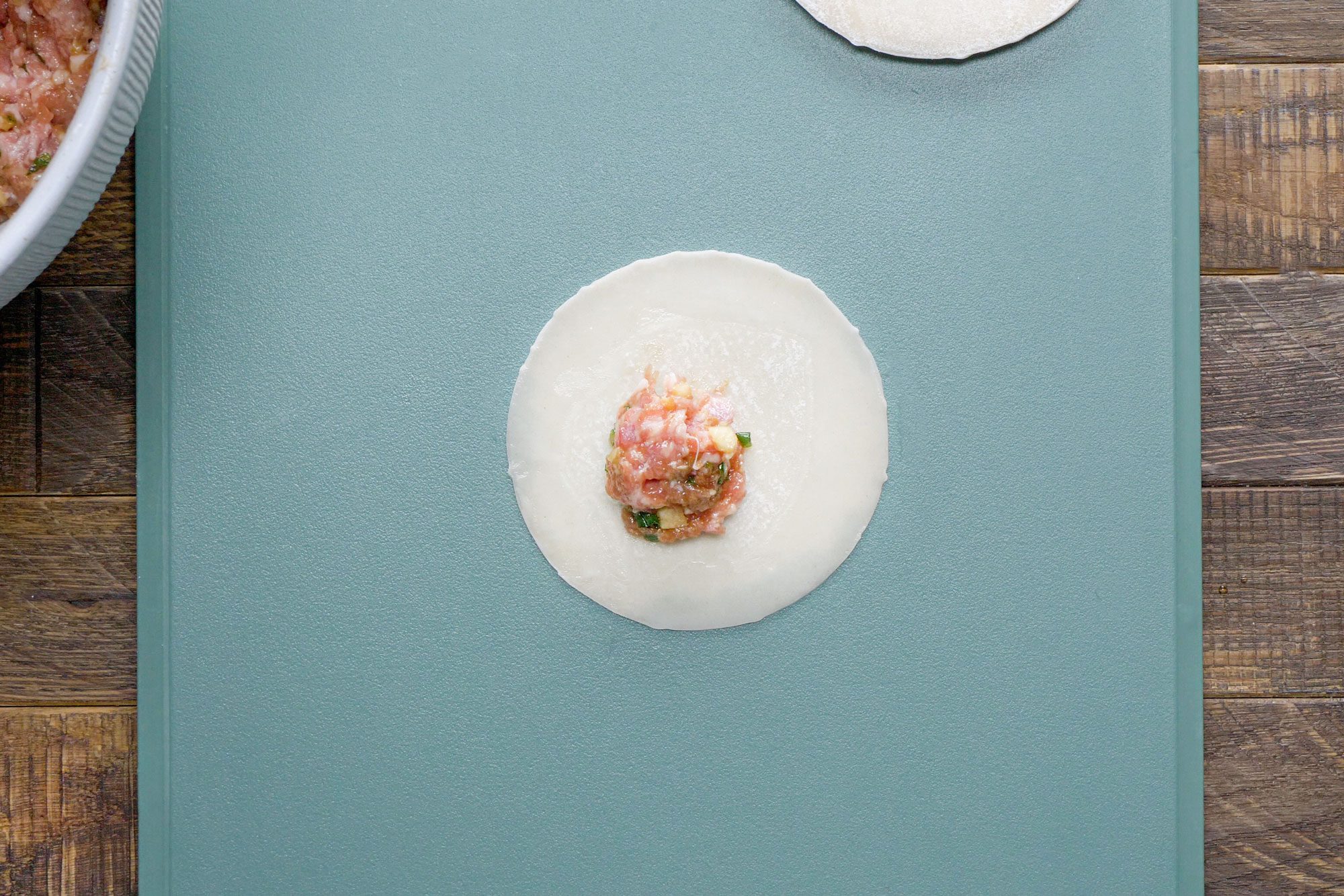 Pork Mixture on Dumpling Wrapper on Chopping Board on Wooden Surface