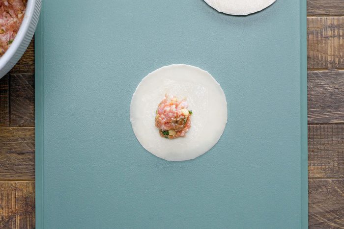 Pork Mixture on Dumpling Wrapper on Chopping Board on Wooden Surface