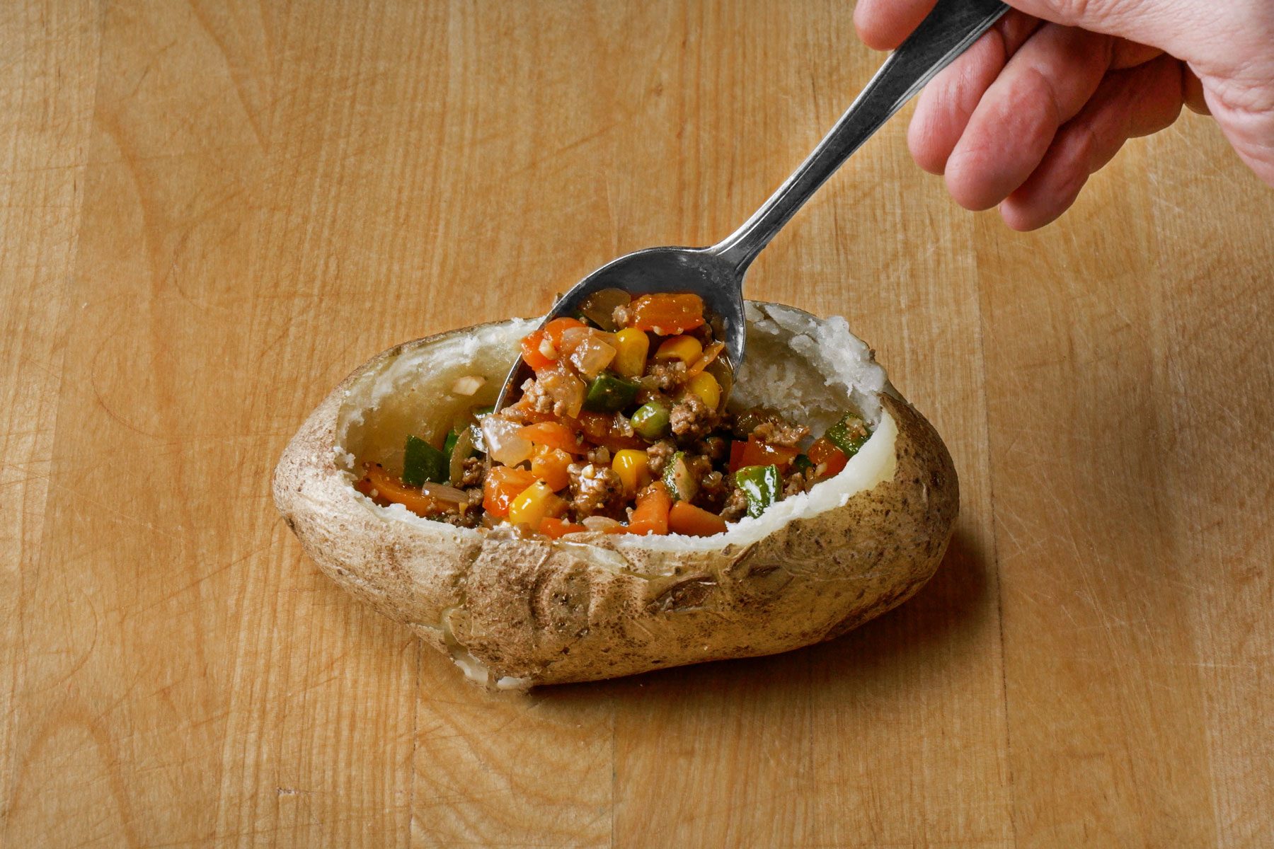 Adding meat mixture into each potato shell with a spoon