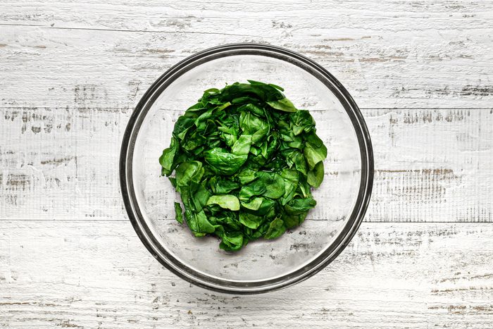 A bowl of wilted spinach over a wooden table.