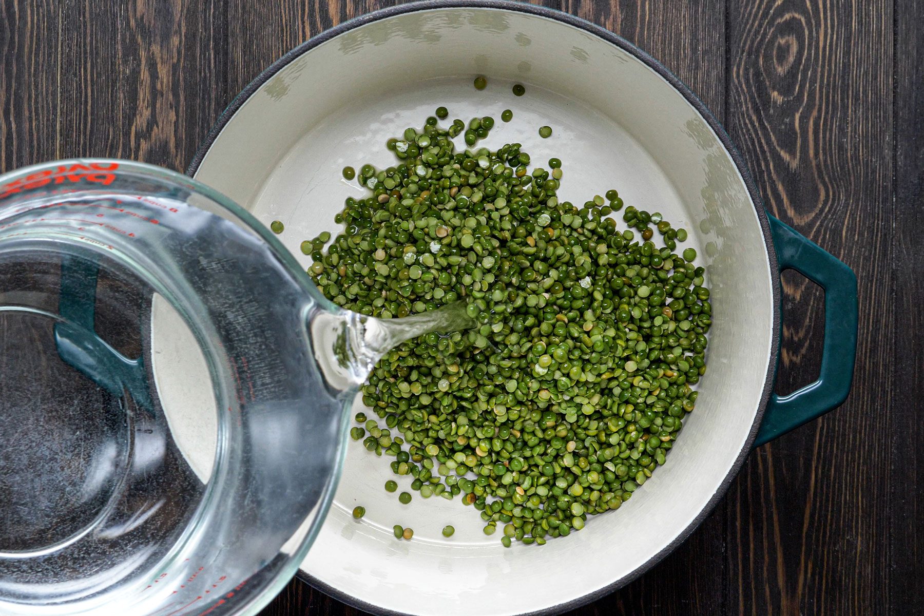 Pouring water on peas in a large pan place on a wooden surface