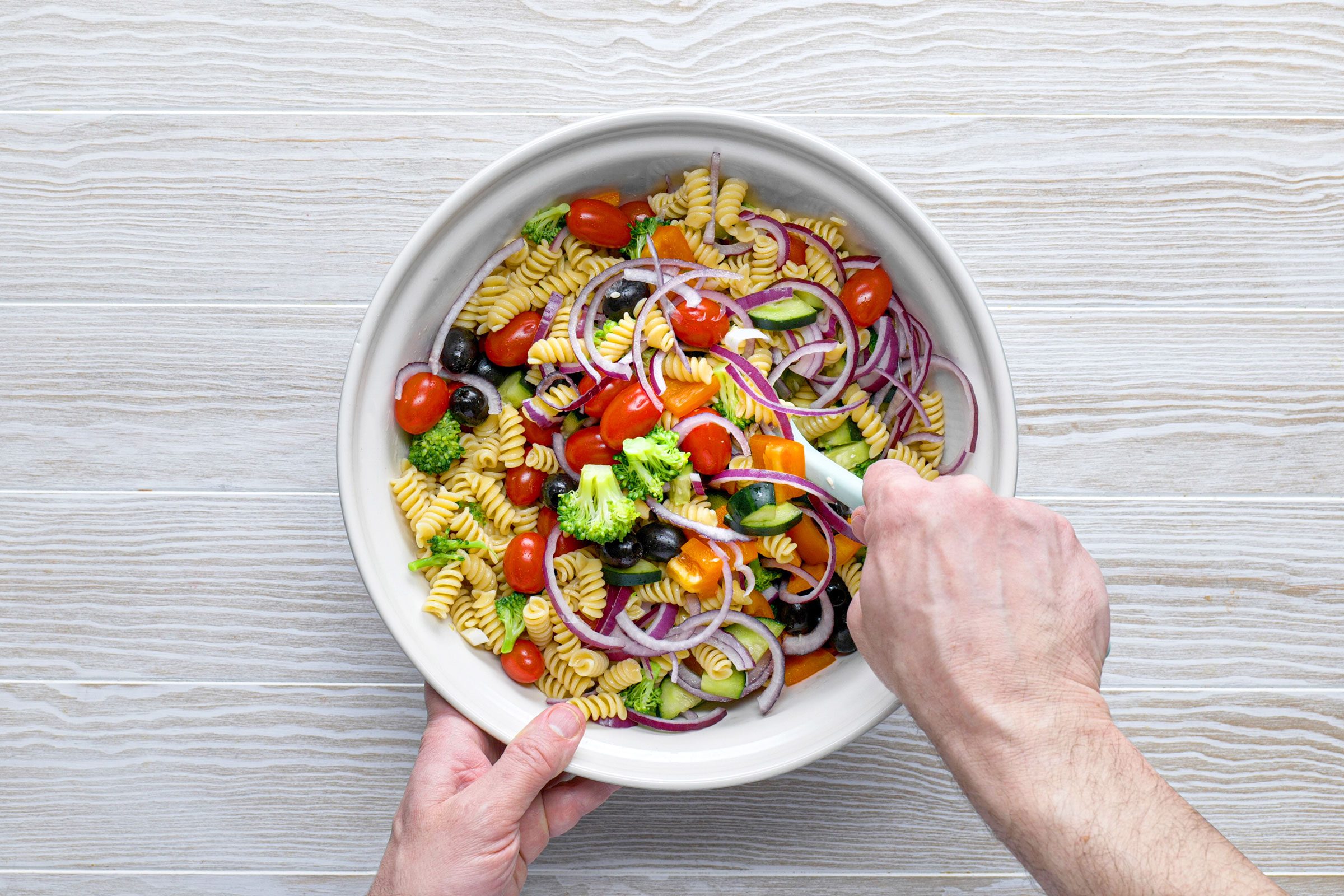 mixing ingredients for pasta salad in a bowl