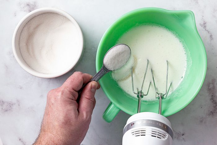 A person adding sugar in mixture in a large green bowl