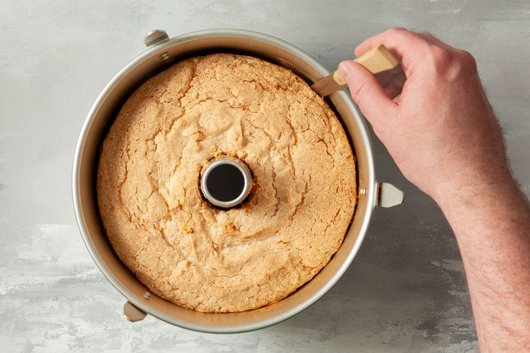 Running a knife through the sides of Angel Food Cake in a pan