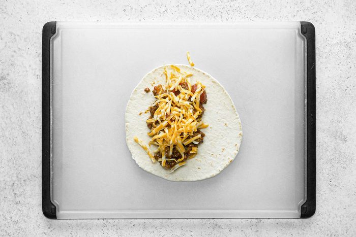 Cheese and sauce on tortillas on table top