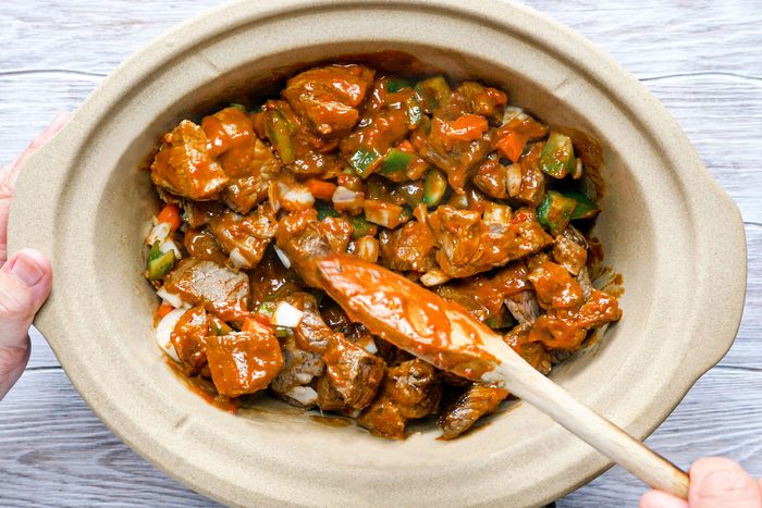 Mixing the meat with sauce in slow cooker using a spatula