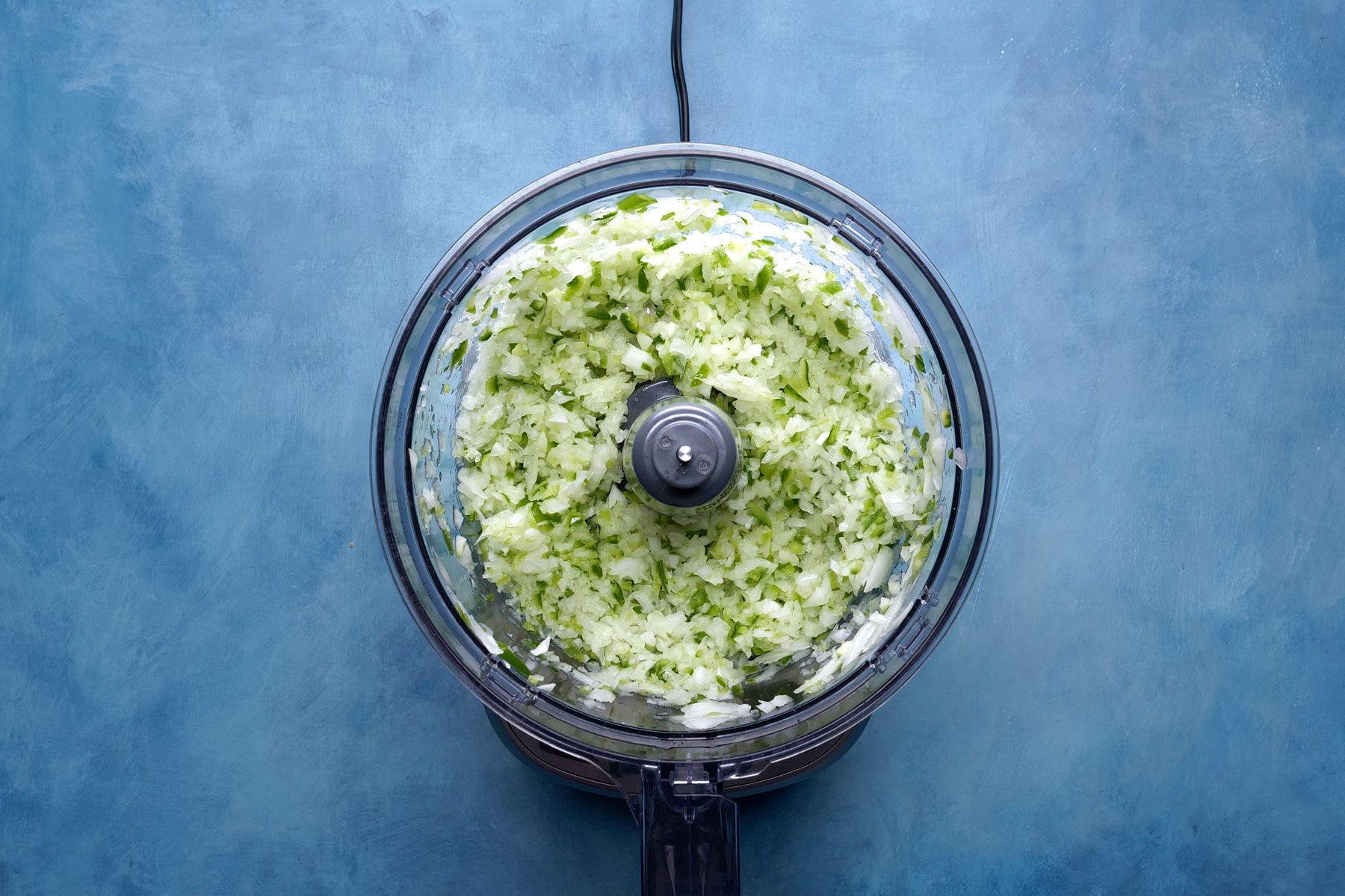 Onion and peppers in a food processor on a countertop