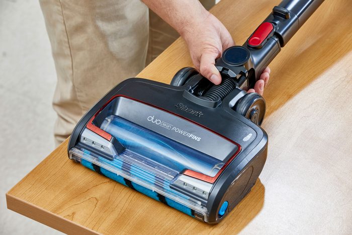 A person holding Shark Vacuum place on a wooden table
