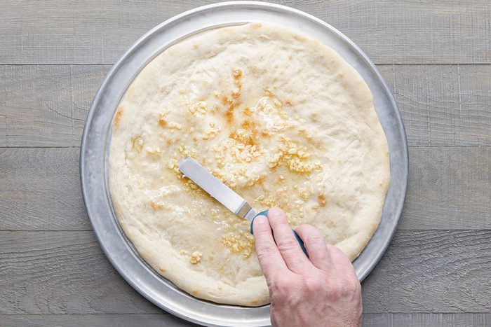 Spreading oil and garlic on pizza base