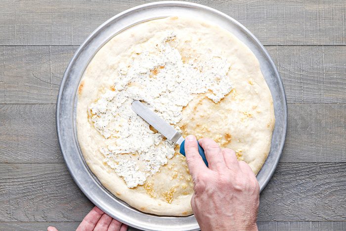 Spreading ricotta mixture over pizza base