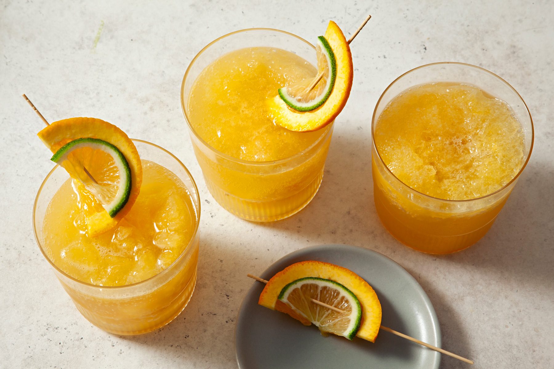 Bourbon Slush served in three glasses garnished with orange and lemon wedge.