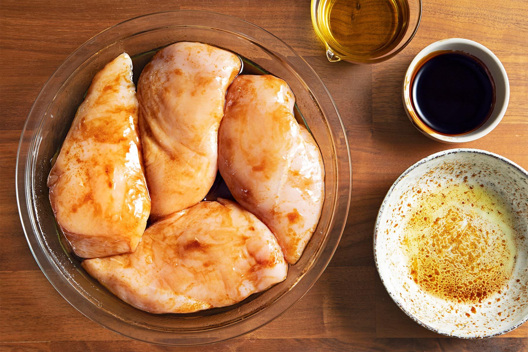 Overhead shot of marinated chicken breats; in a shallow dish; oil; balsamic glaze; salt; brown wooden background;