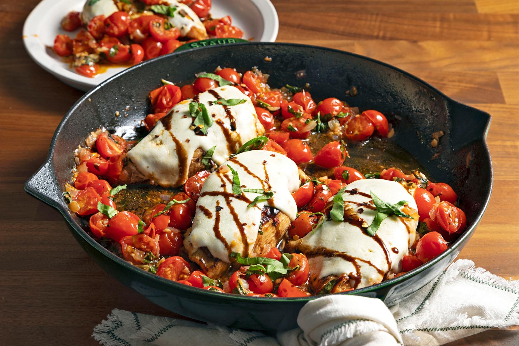 3/4 angle view shot of Baked Bruschetta Chicken; in large skillet; served on plate; cloth; brown wooden background;