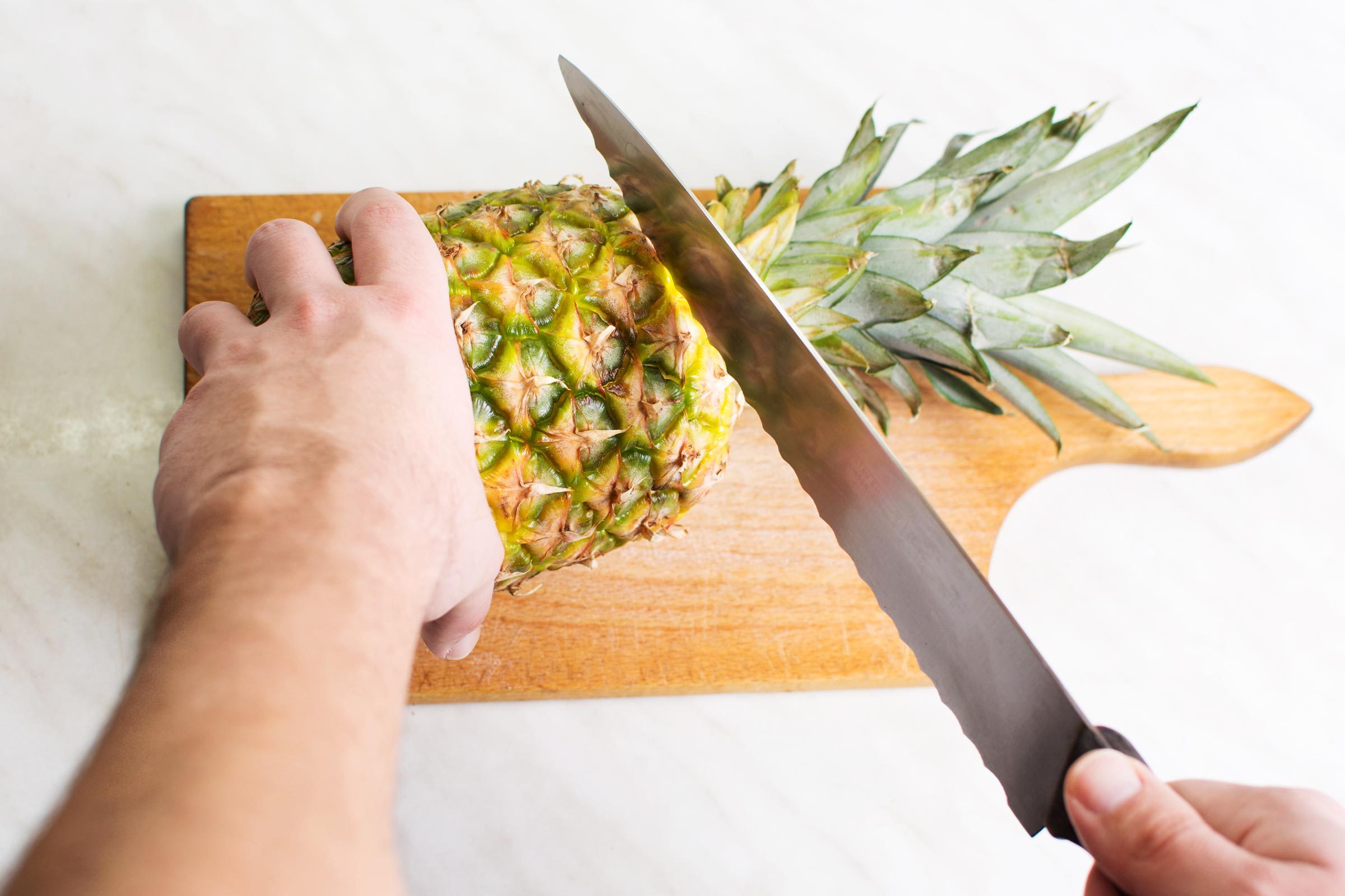 hand cutting the top off of a pineapple