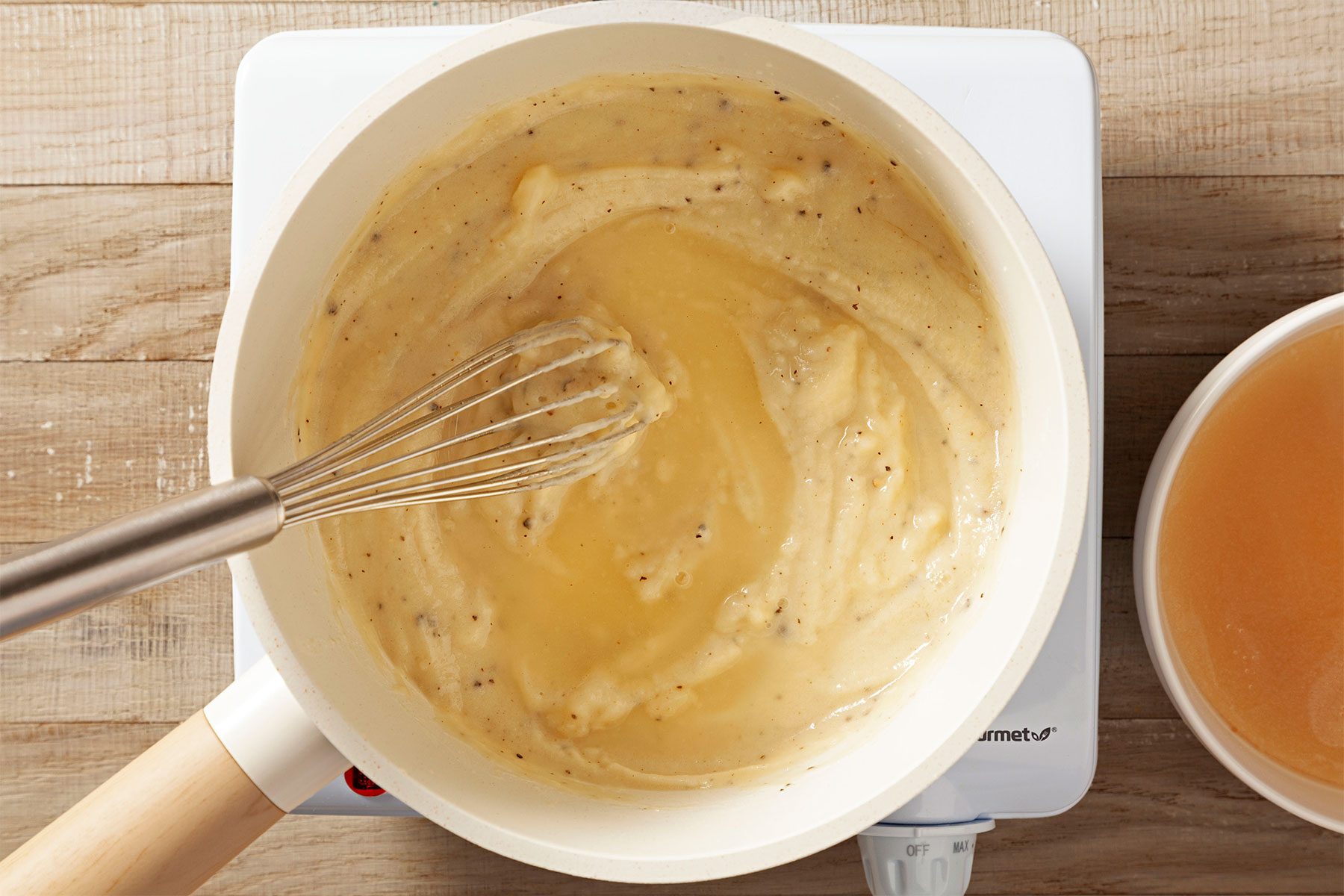 Overhead shot of gradually whisk in ham base mixture; whisk tool; induction stove; wooden background;