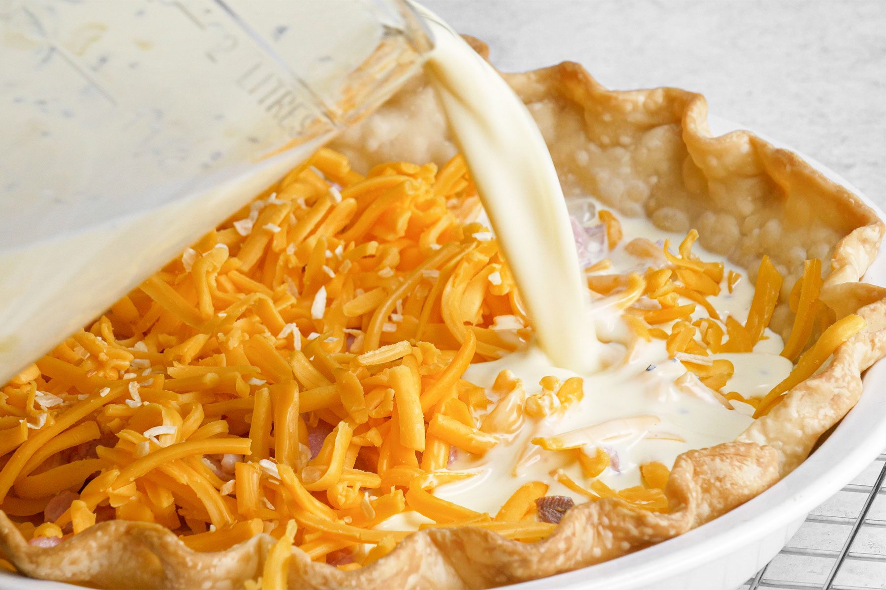 Pouring white sauce over Ham And Cheese Quiche