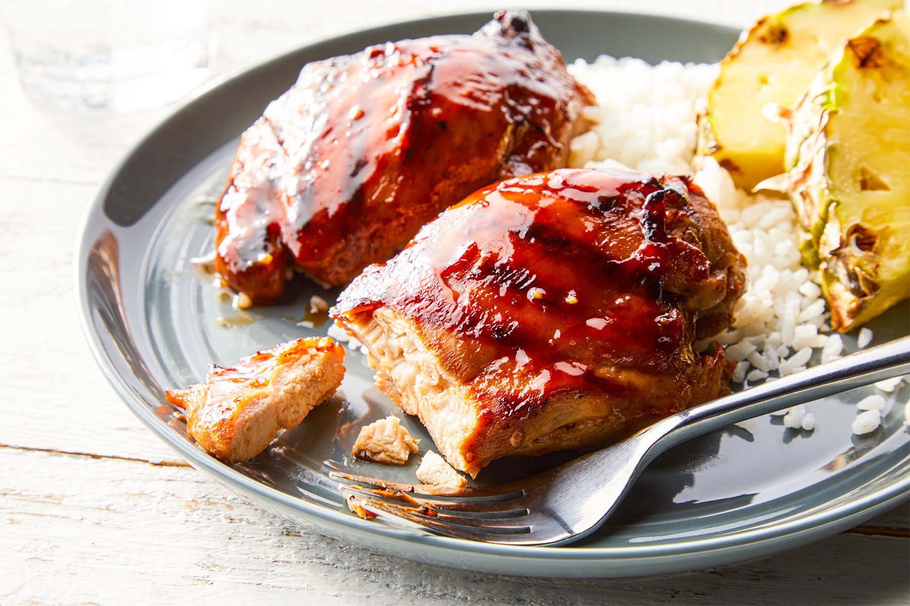 3/4 angle view shot of Grilled Huli Huli Chicken; served on large platter; fork; rice bowl; napkin; white wooden background;
