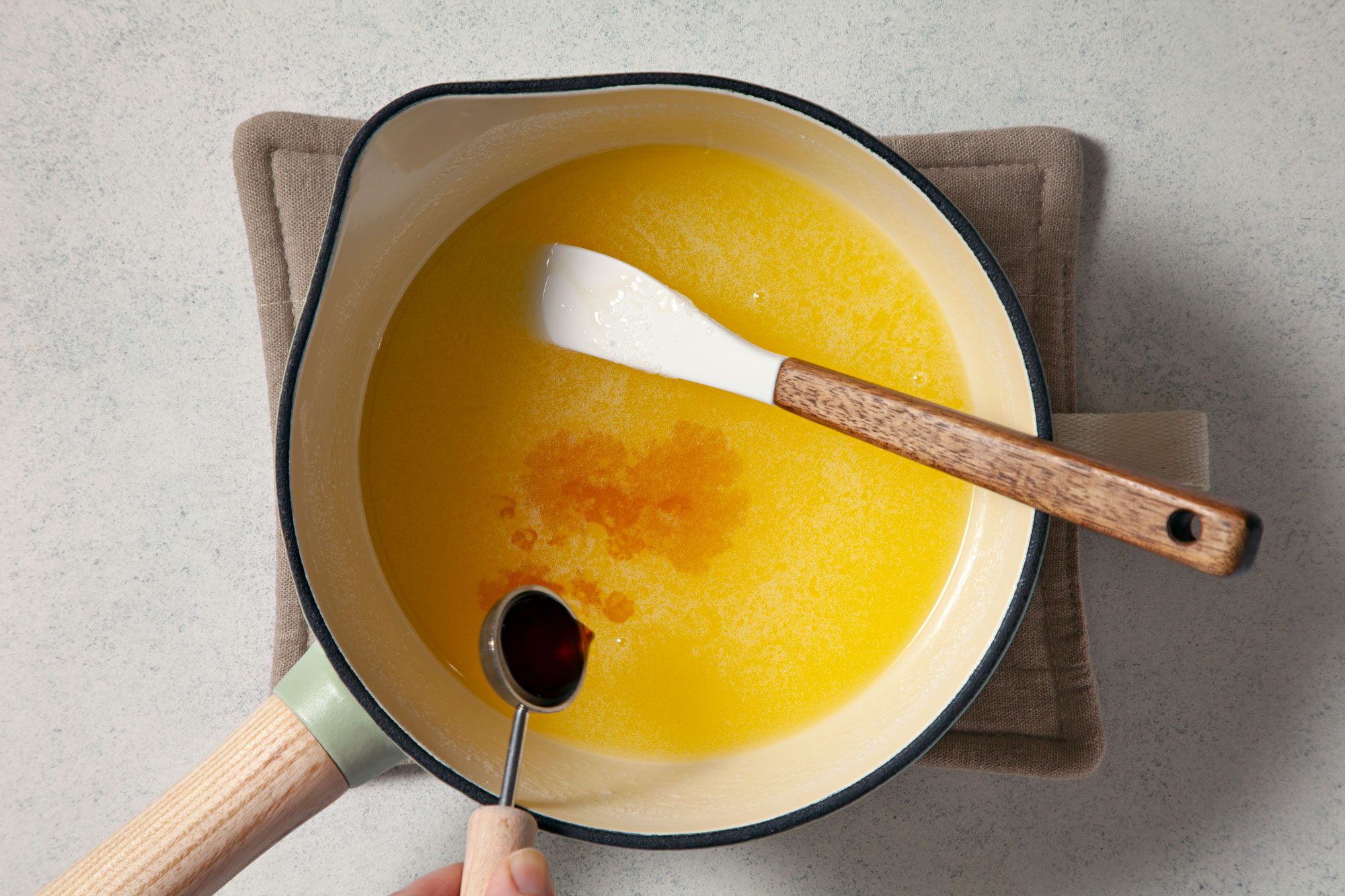 overhead shot of adding vanilla extract in melted sugar and butter in a small saucepan