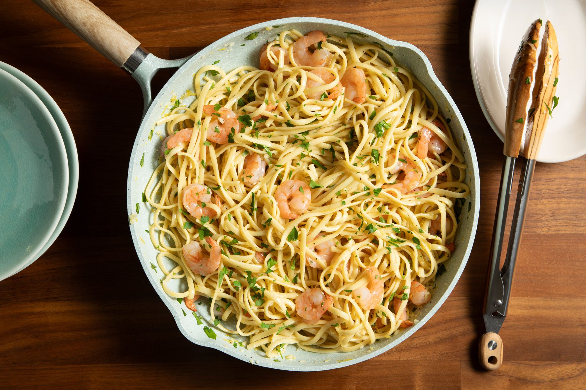 overhead shot; wooden background; Garlic-Lemon Shrimp Linguine in large white pan with tongs