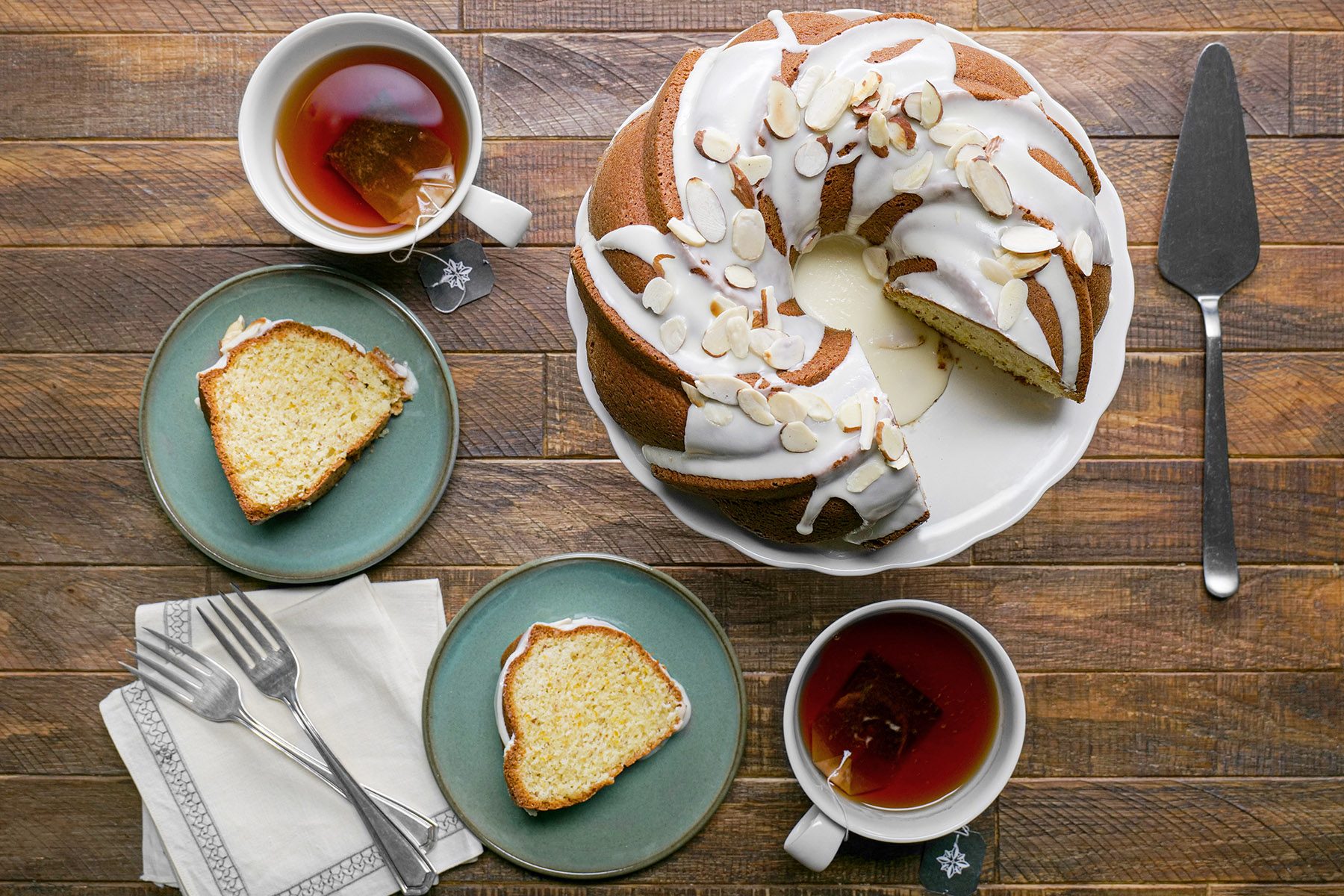 Overhead shot of Olive Oil Cake sprinkle with almonds served with tea cake knife forks plates napkin wooden background