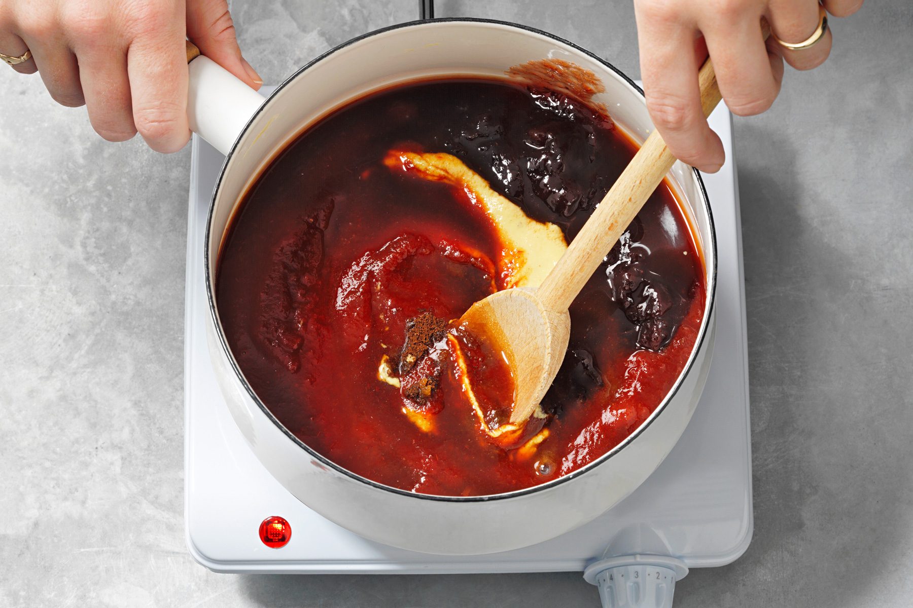 A hand is mixing sauce with other ingredients in a saucepan