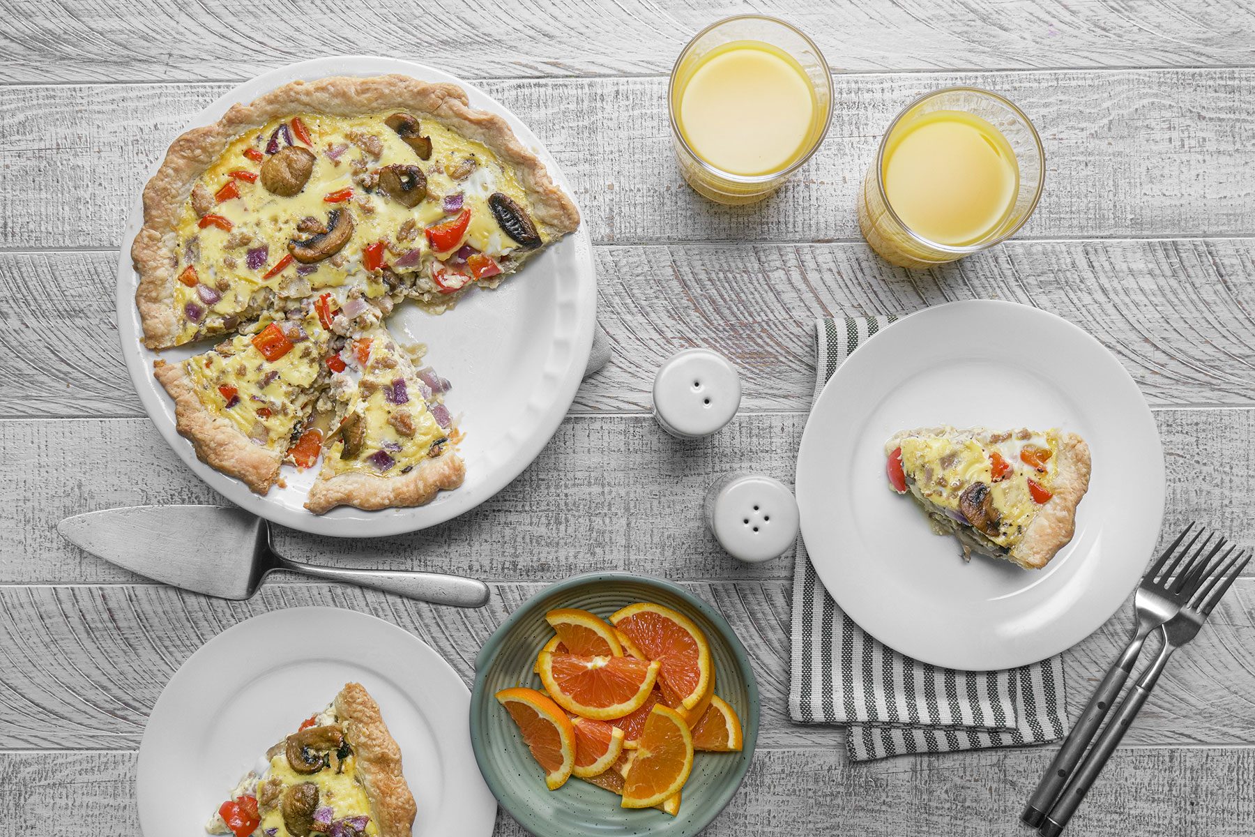 Quiche served on plate with orange juice and slices of oranges