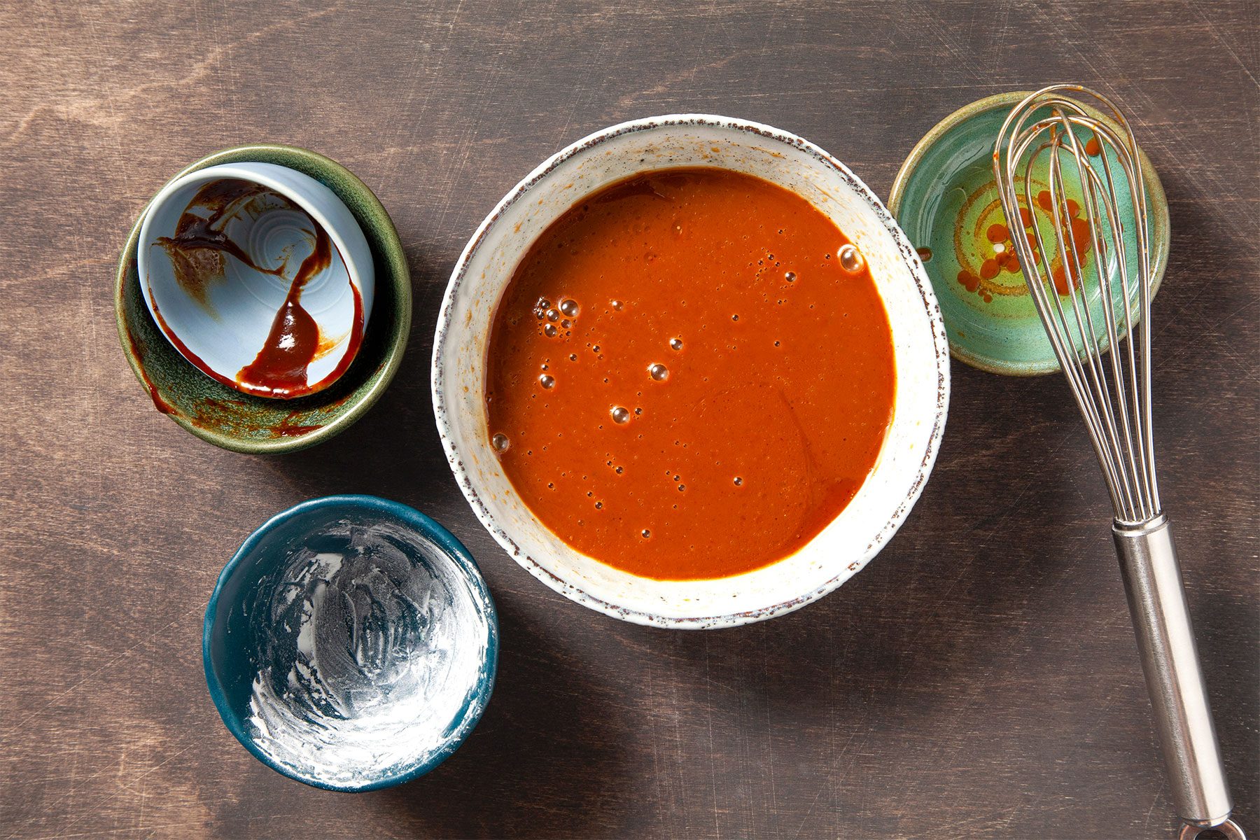 Red sauce mixture ion large bowl with two other bowls on the side