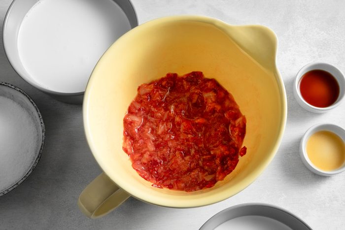 Overhead shot of mashed strawberries in a large bowl on white marble background