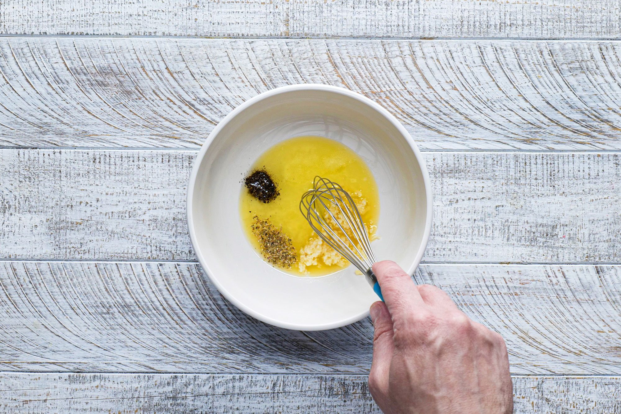 overhead shot; white wooden background; stiring egg yolk and other spices using whisker;
