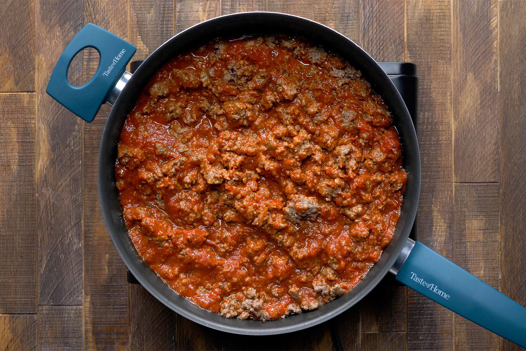 overhead shot of beef cooked in spagetti sauce in a large pan; wooden surface;