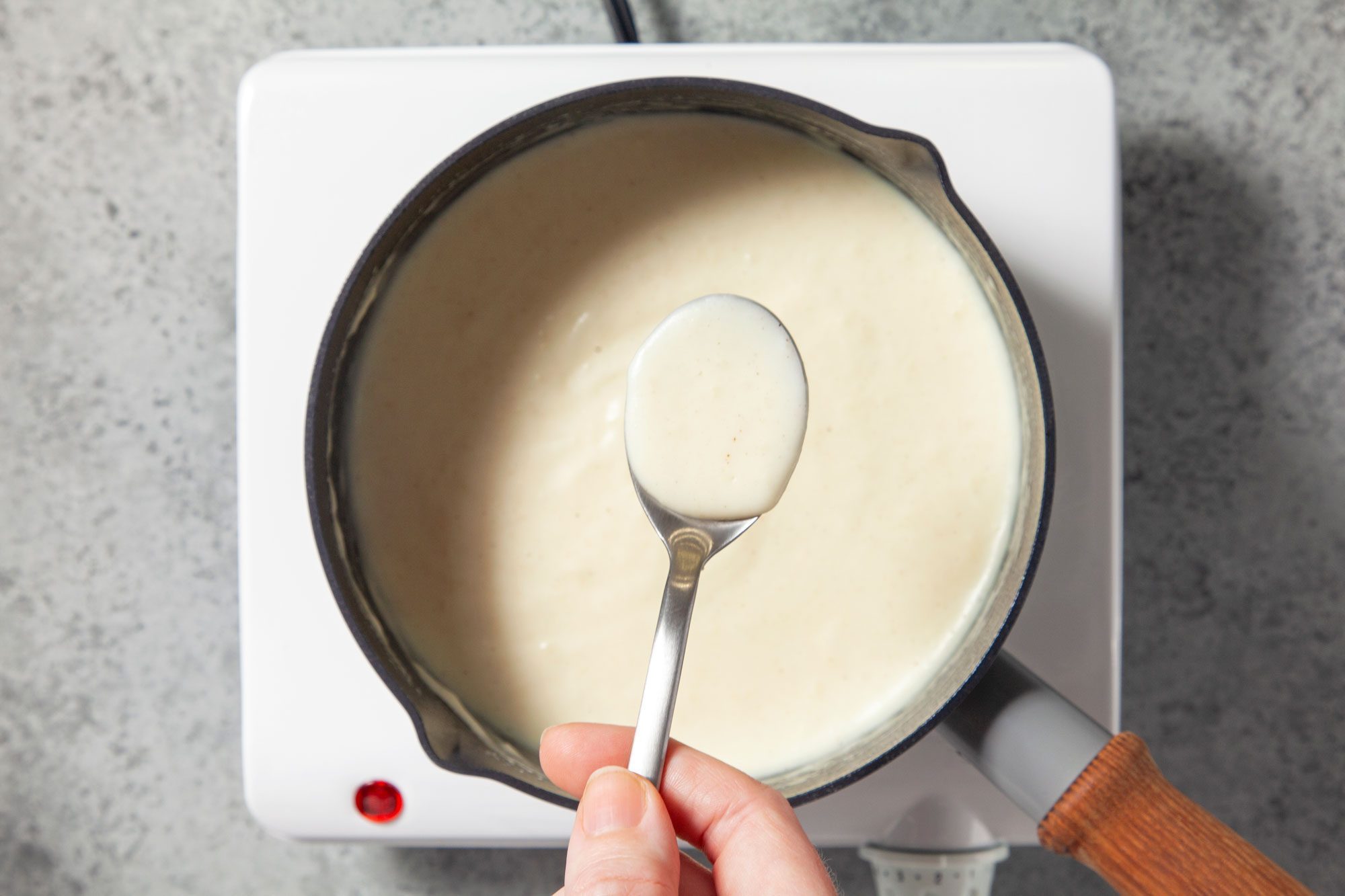 Overhead shot of cook and stir basic white sauce until thickened; spoon; induction; marble background;