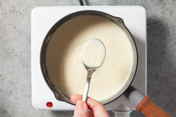 Overhead shot of cook and stir basic white sauce until thickened; spoon; induction; marble background;