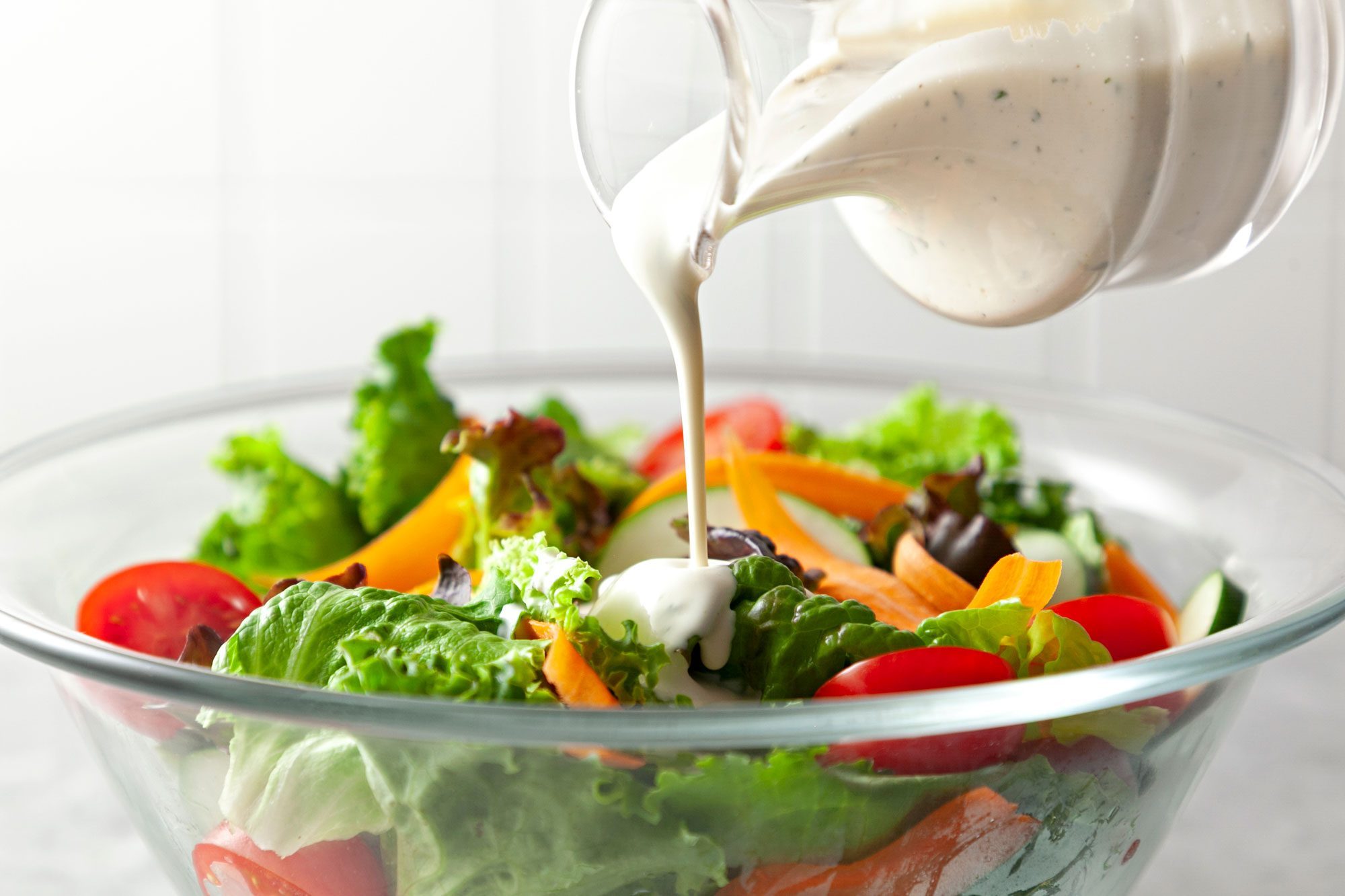 Pouring Basic Buttermilk Salad Dressing over salad in glass bowl