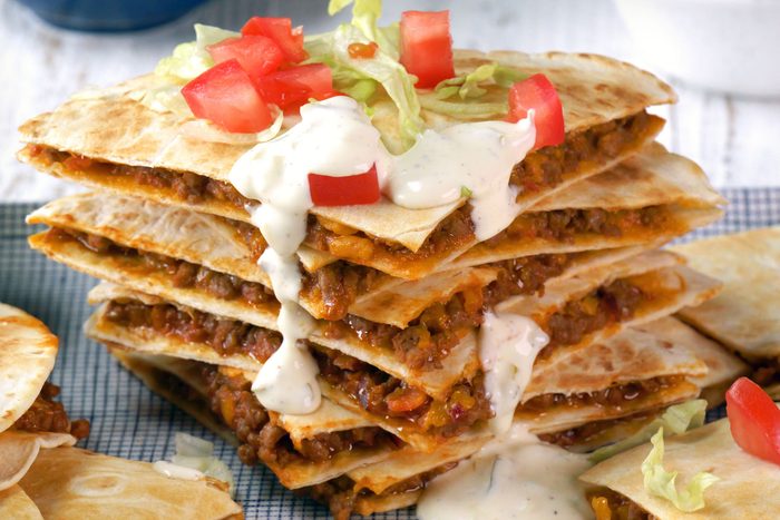 close shot of cheeseburger quesadillas served with shredded lettuce and chopped tomatoes