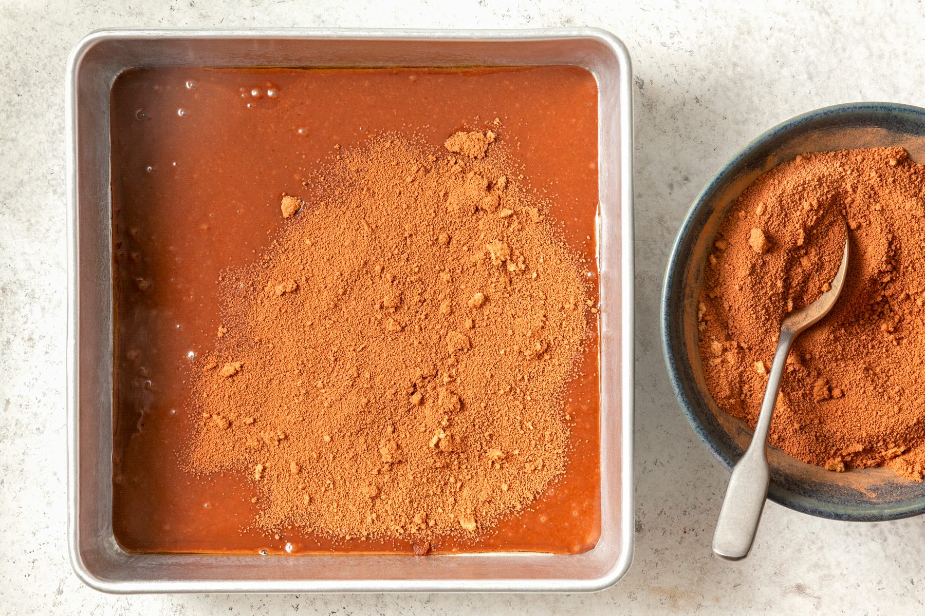 A baking pan filled with chocolate batter sprinkled with cocoa powder
