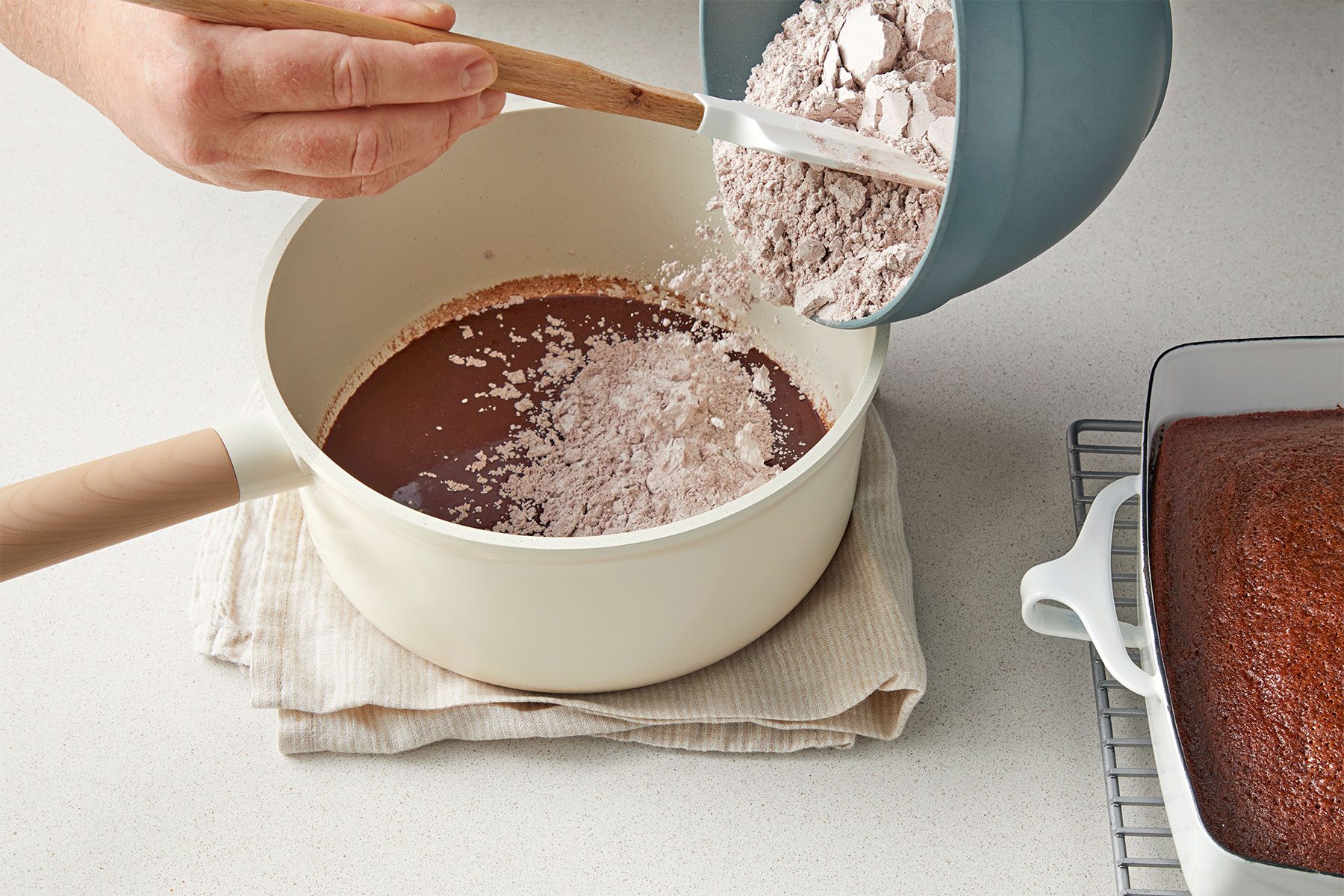 high angle shot of flour mix added in the cola and cocoa batter in a saucepan